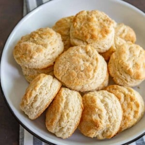 A white plate filled with golden-brown, freshly baked biscuits—made from an easy homemade biscuit recipe—sits on a black and white striped cloth.