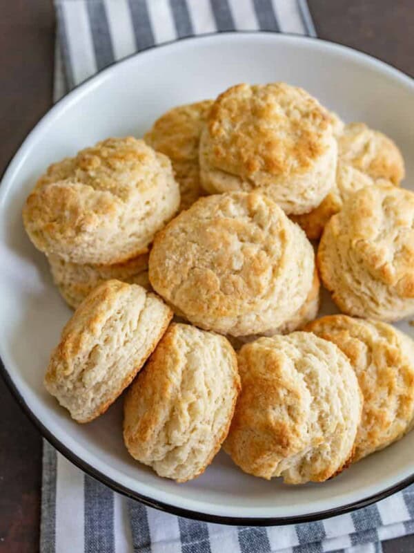 A white plate filled with golden-brown, freshly baked biscuits—made from an easy homemade biscuit recipe—sits on a black and white striped cloth.