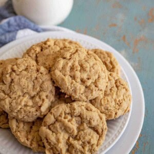 A white plate stacked with several easy oatmeal cookies sits on a rustic blue surface, with a glass of milk in the background.