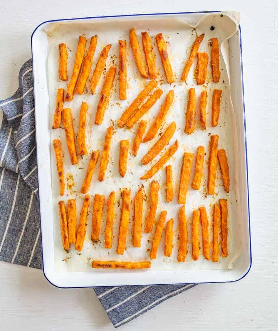 Image of sweet potato fries, cooked, on a white enamel baking sheet with a blue rim looking down from the top. 