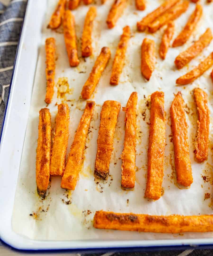 Image of cooked sweet potato fries on a parchment paper on a baking sheet.