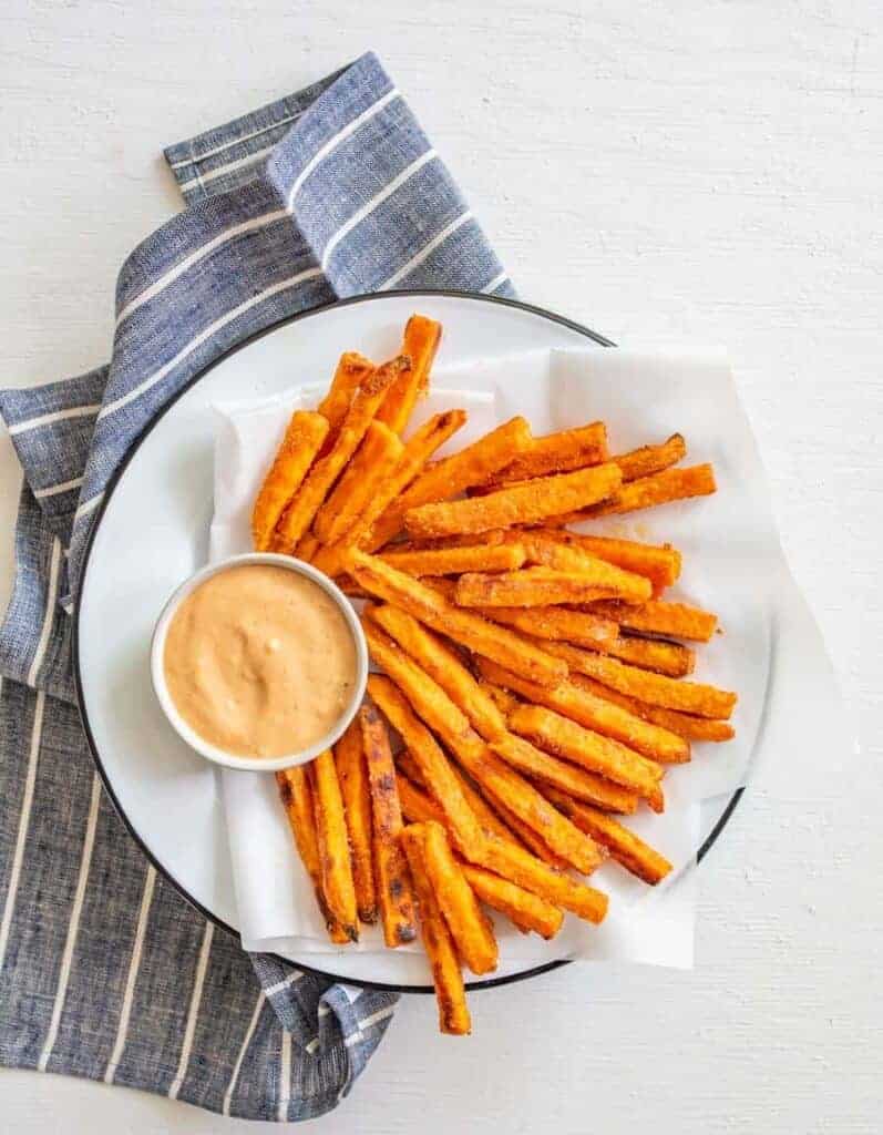 sweet potato fries on a white serving plate with a light red dipping sauce in a round white bowl