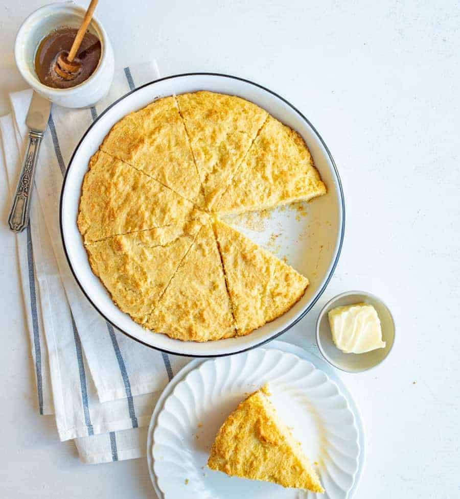 sour cream cornbread in round white dish with piece cutout on white plate with butter and honey