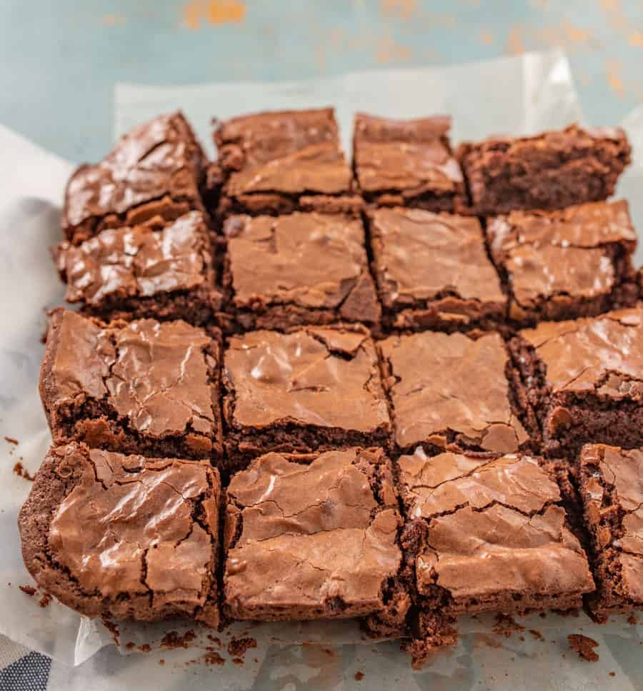 A close-up of a pan of brownies cut into 16 on a piece of white parchment paper. 