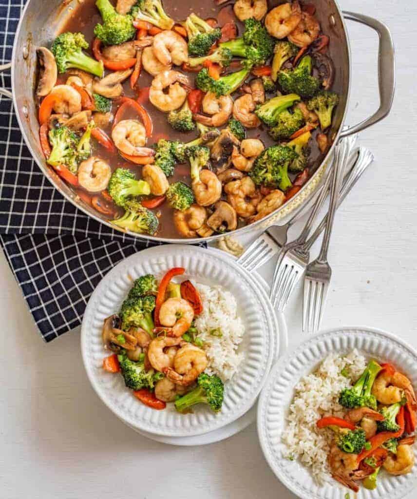 shrimp stir fry in the pan it's made in plus 2 serving bowls with a portion in each with rice