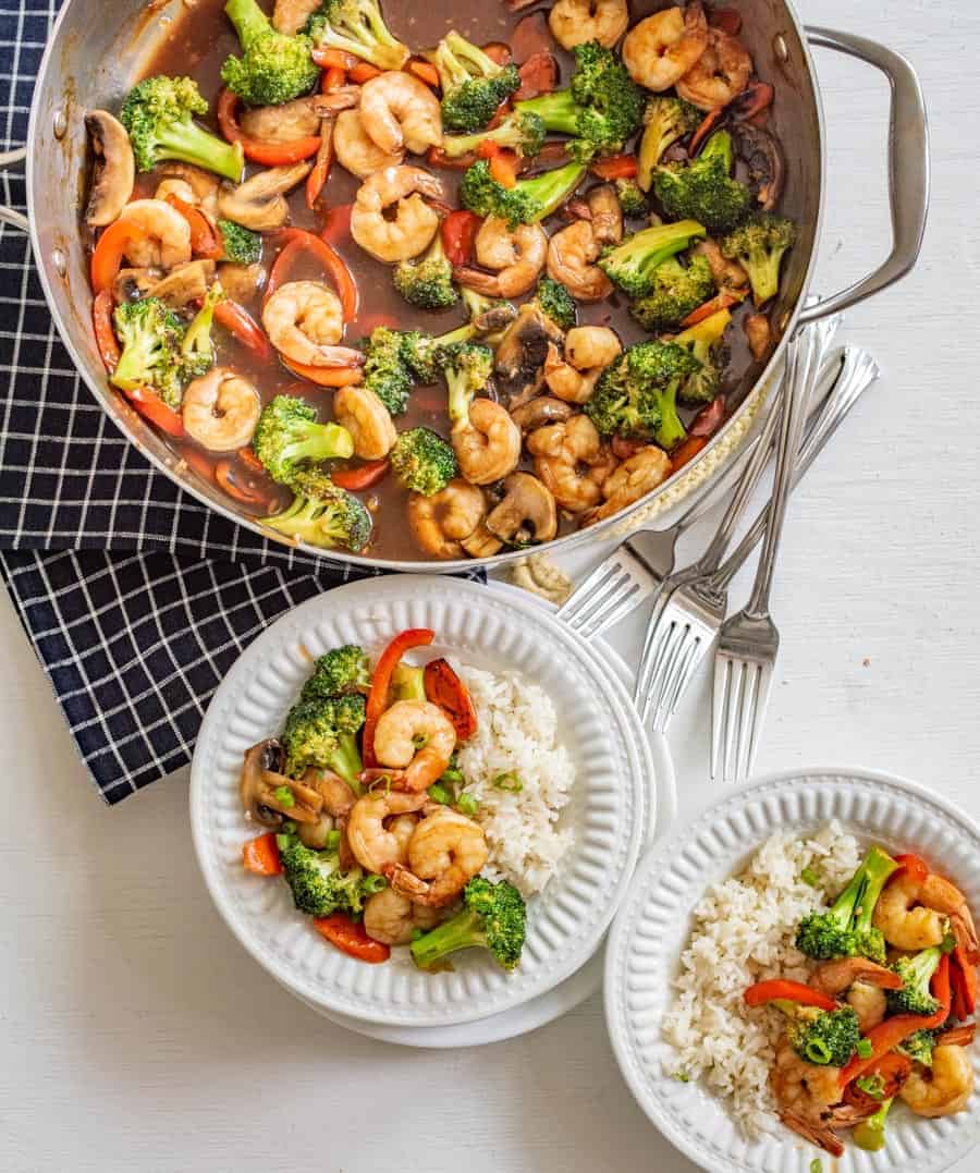 shrimp stir fry in the pan it's made in plus 2 serving bowls with a portion in each with rice