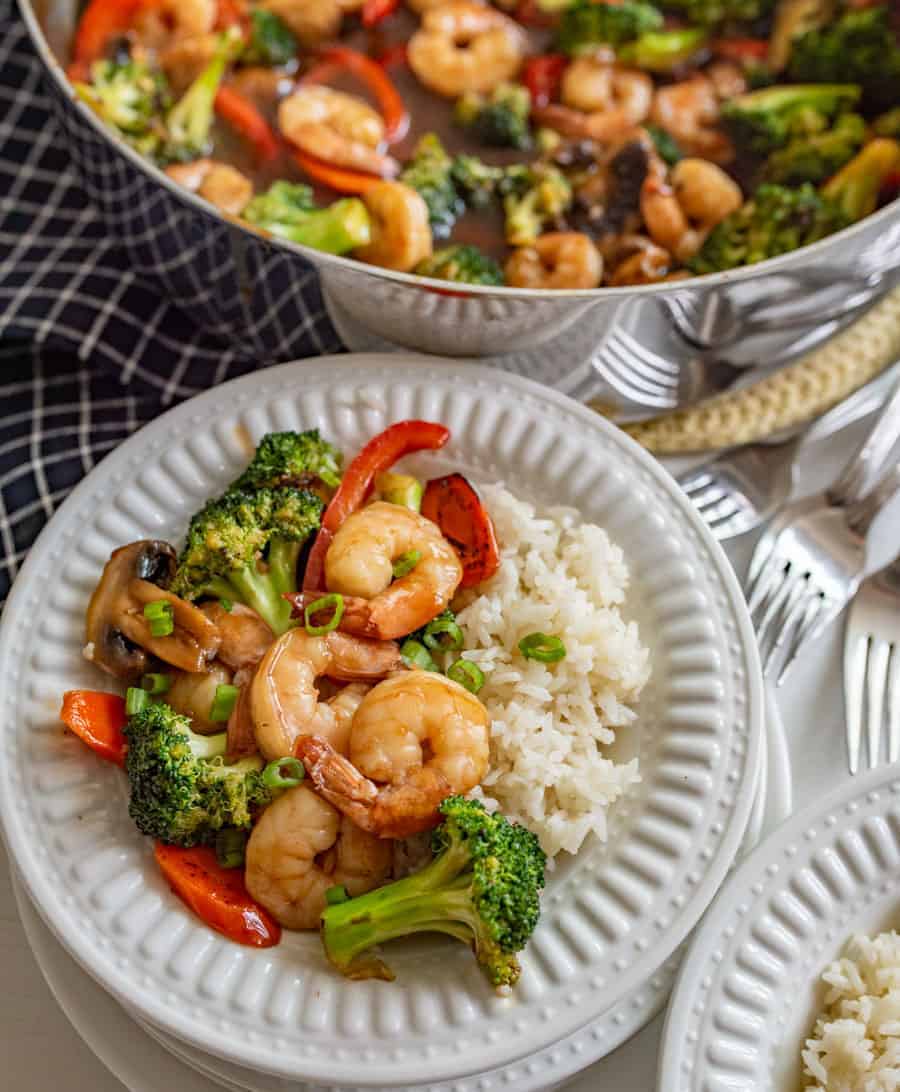 shrimp and veggies with white rice on white plate next to pot of shrimp and vegetables and forks