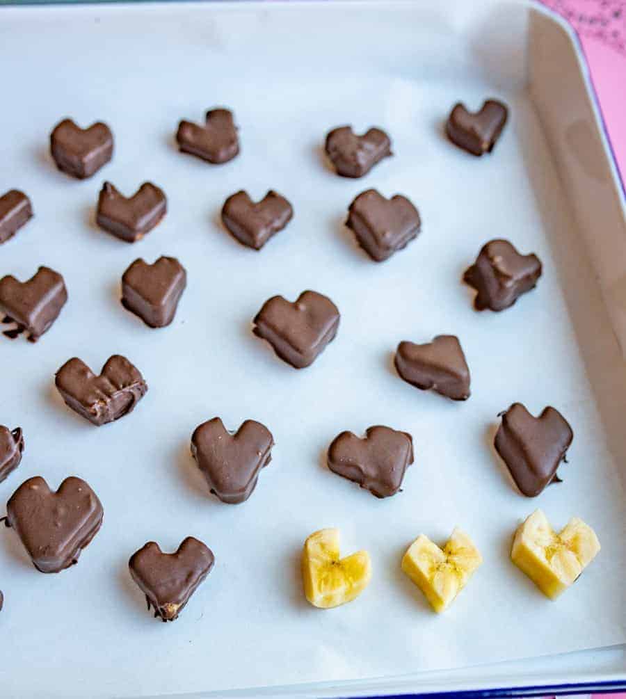 Slices of banana dipped in chocolate on a cookie sheet with parchment paper.