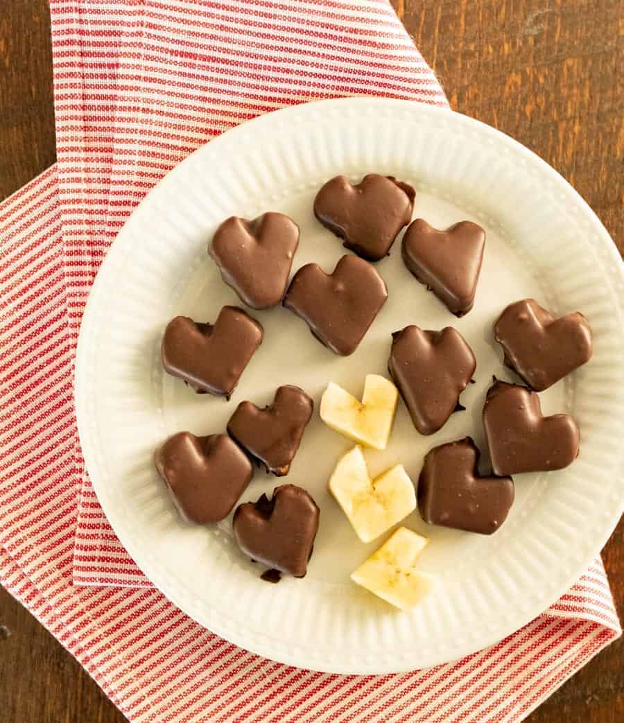 Chocolate covered banana hearts on a white plate on top of a red and white striped napkin. 