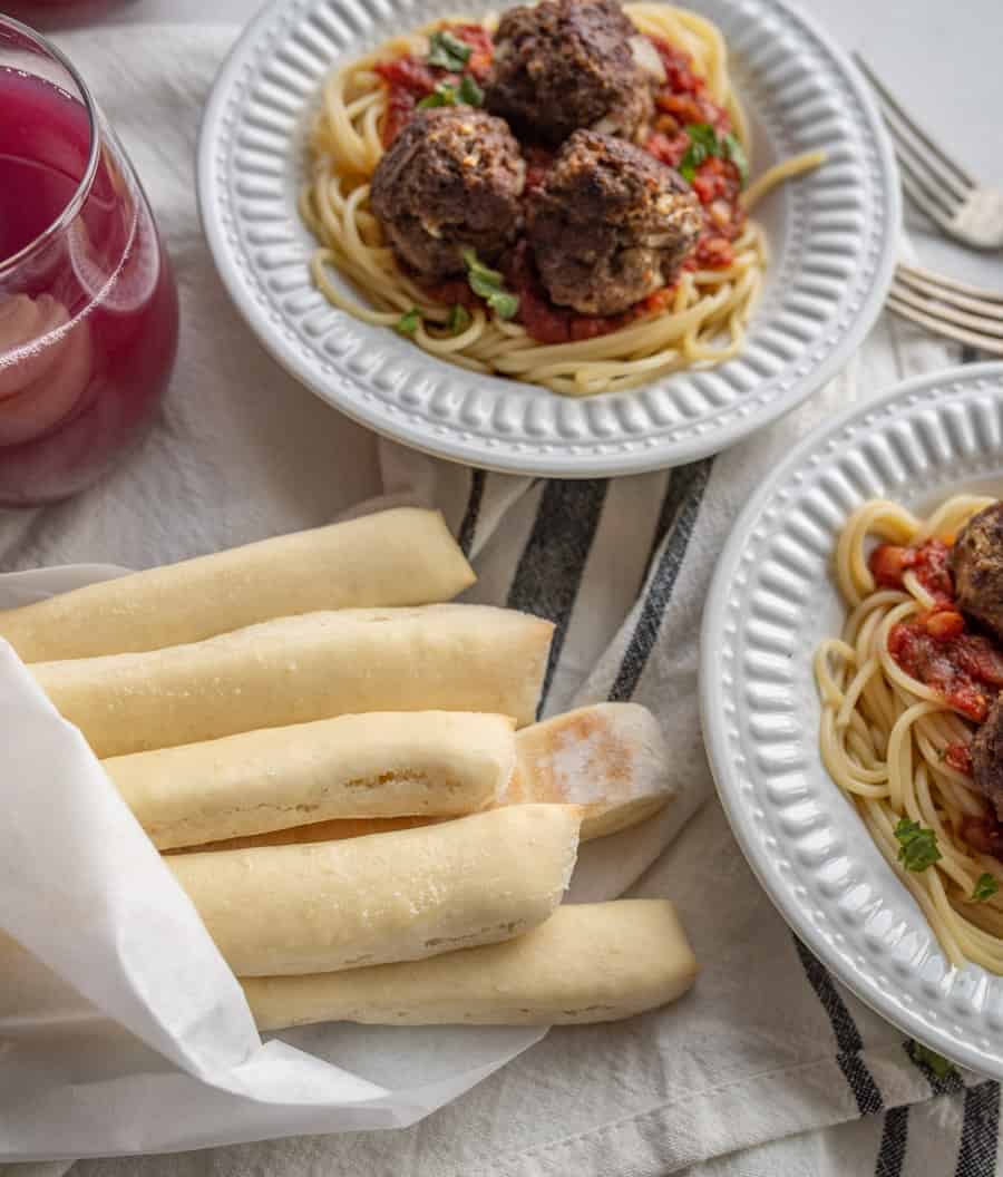 on overhead shot of breadsticks wrapped in parchment paper being served alongside spaghetti and meatballs.