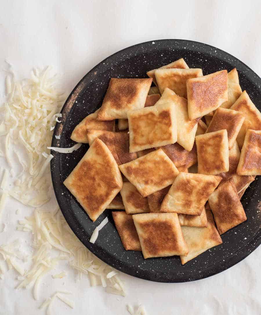 Baked fathead crackers on a black plate with white speckles on a white counter with some shredded mozzarella in the background. 