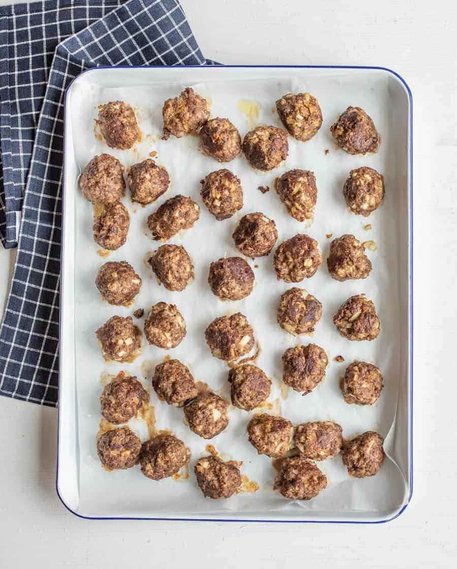 Cooked meatballs on a baking sheet after coming out of the oven.