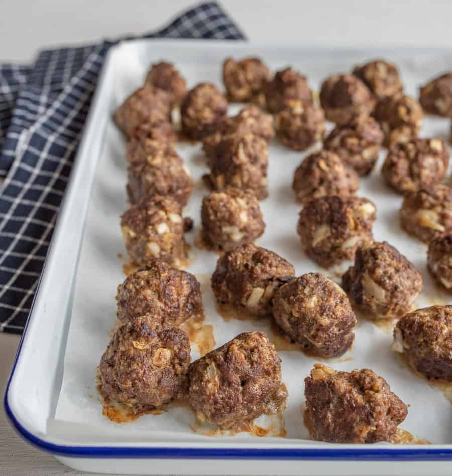 Cooked meatballs on a blue-rimmed white baking sheet after coming out of the oven.