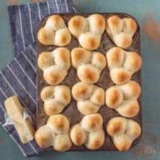 Grandma Lucy's famous clover rolls in muffin pan on white striped blue towel next to stick of butter.