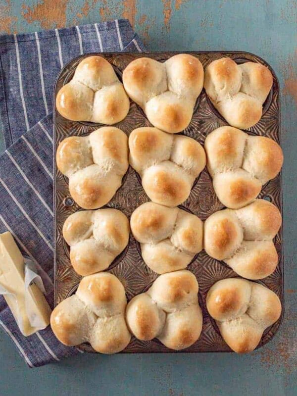 Grandma Lucy's famous clover rolls in muffin pan on white striped blue towel next to stick of butter.