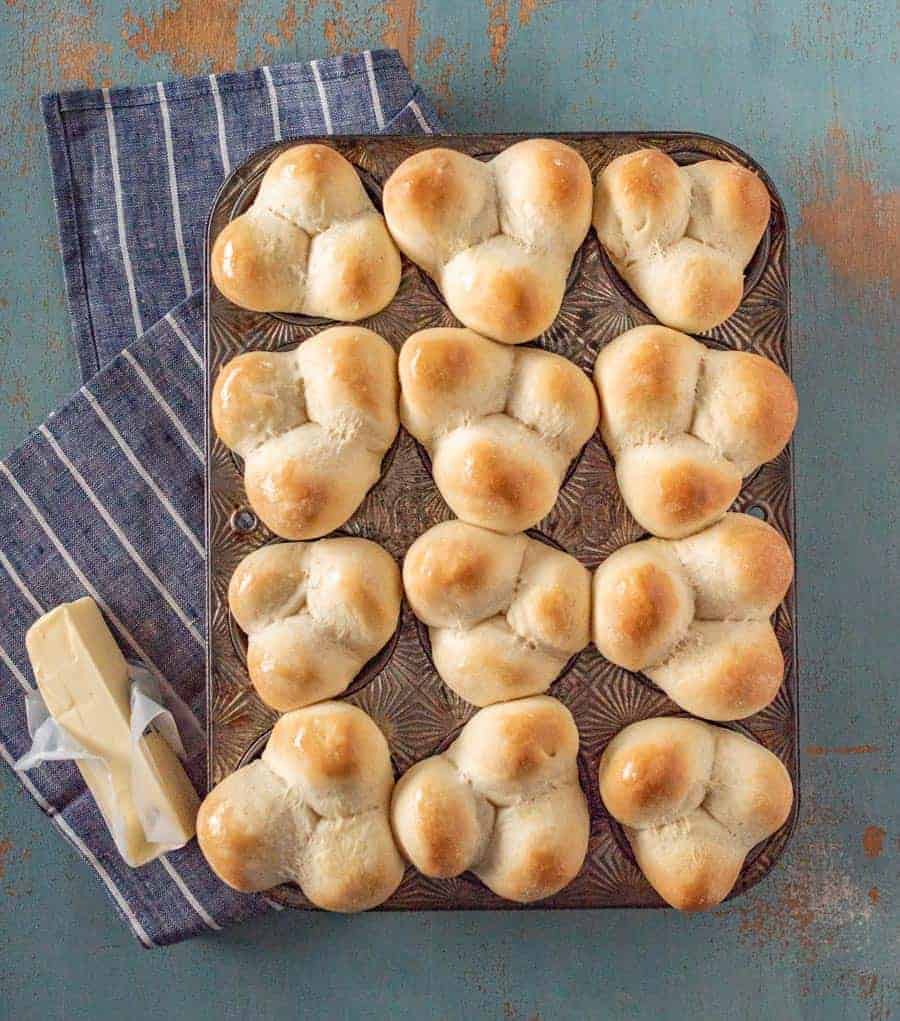 Grandma Lucy's famous clover rolls in muffin pan on white striped blue towel next to stick of butter.