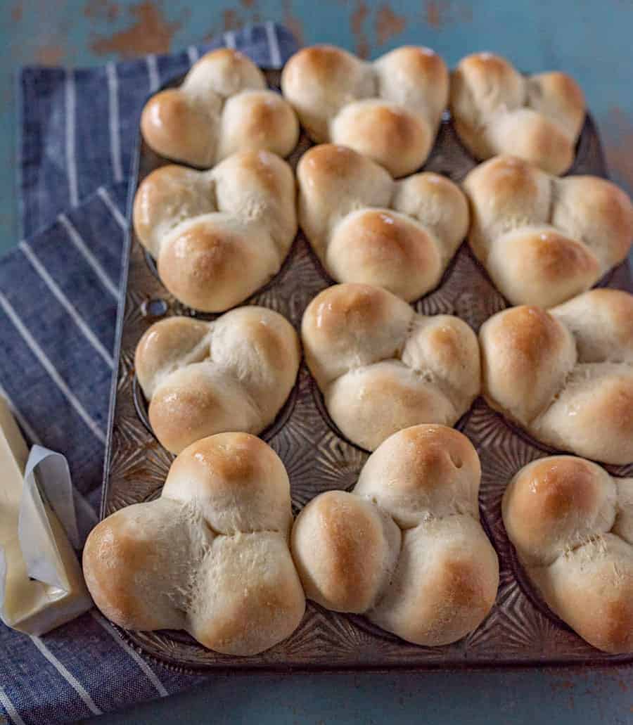 Grandma Lucy's famous clover rolls in muffin pan on white striped blue towel next to stick of butter.