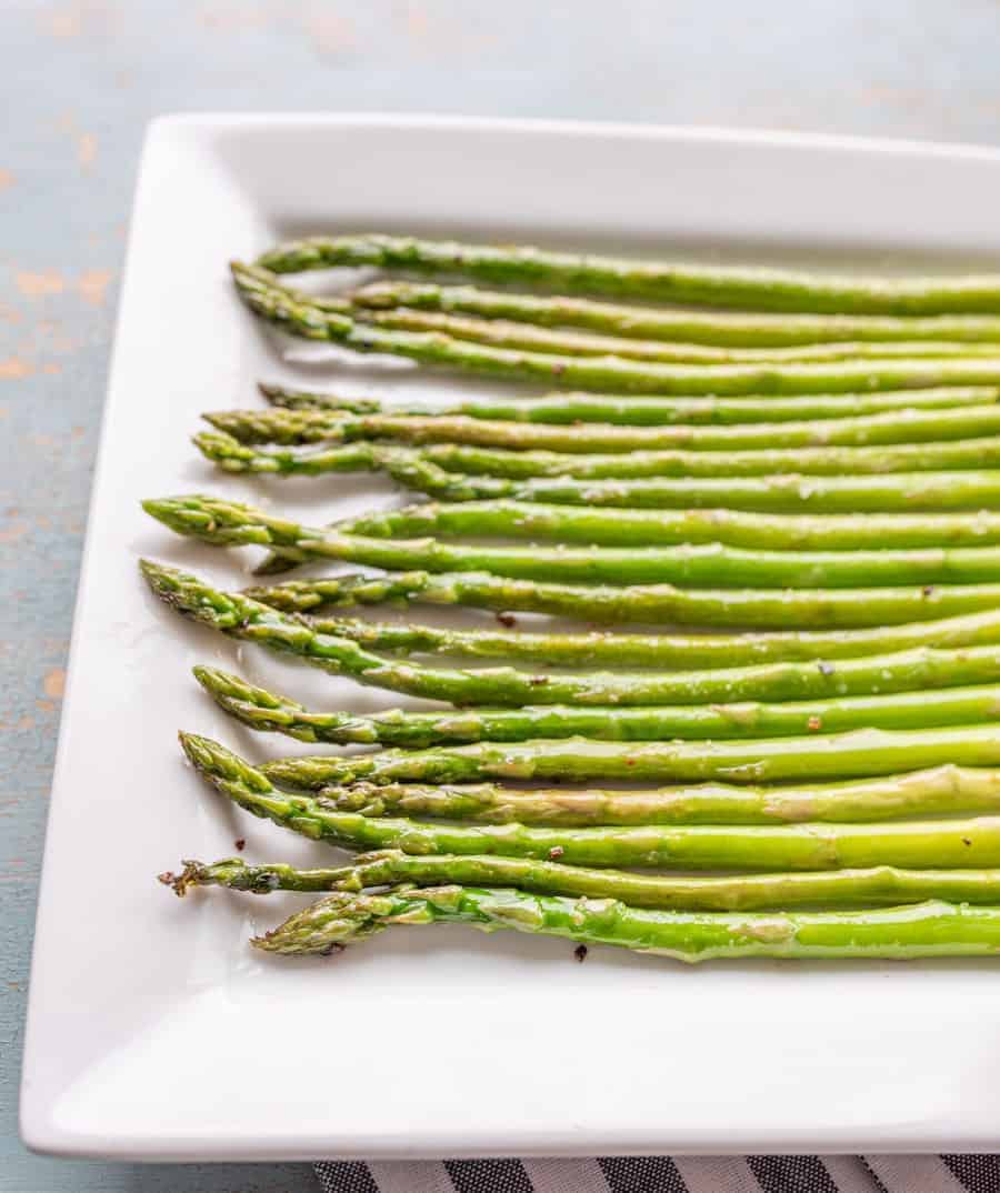 Bright green crisp cooked asparagus on a white plate shining with a bit of cooking oil and sprinkled with salt and pepper.