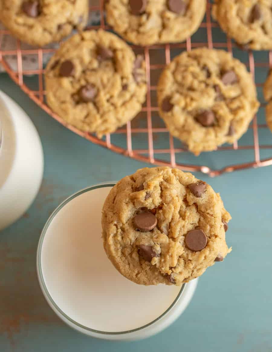copper colored cooling rack with chocolate chip cookies and a glass of white milk with cookie on edge.