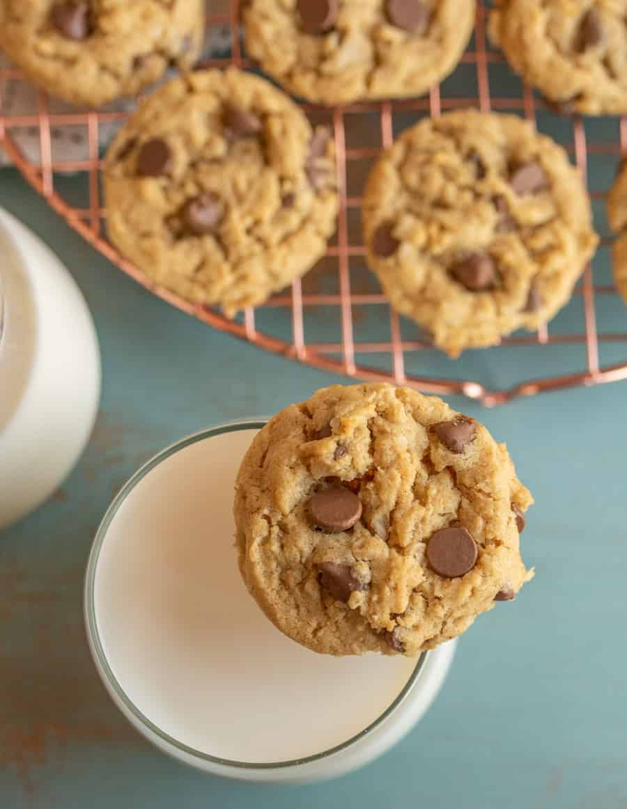 a peanut butter chocolate chip oatmeal cookie resting on the top of a full glass of milk.