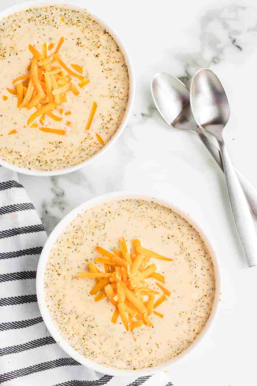 overhead shot of two bowls of cheesy broccoli soup topped with shredded cheese.