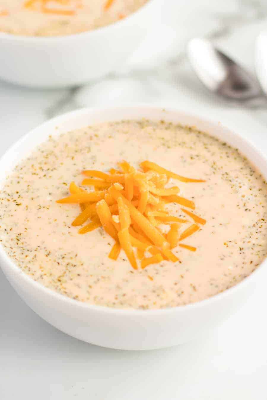 a bowl of cheesy broccoli soup topped with a little bit of grated cheddar cheese.