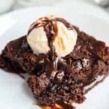 chocolate brownie dessert on a white plate with pale vanilla ice cream scoop on top and a drizzle of chocolate sauce.