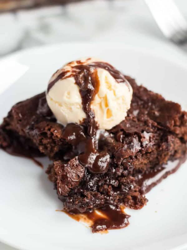 chocolate brownie dessert on a white plate with pale vanilla ice cream scoop on top and a drizzle of chocolate sauce.