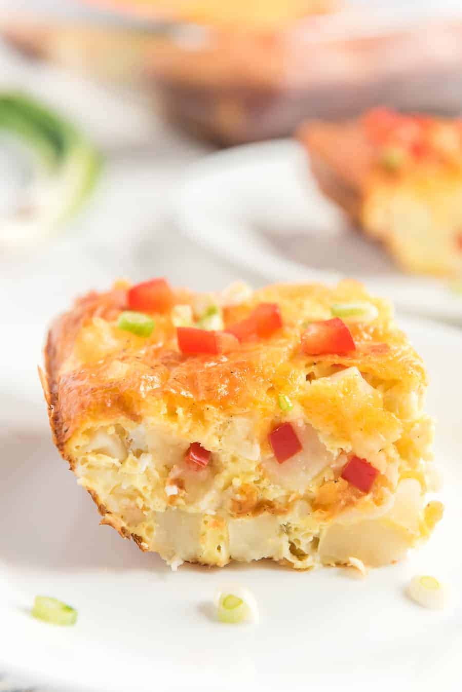 piece of egg and potato breakfast casserole on a spatula with little pieces of red pepper and green onions sprinkled on top.