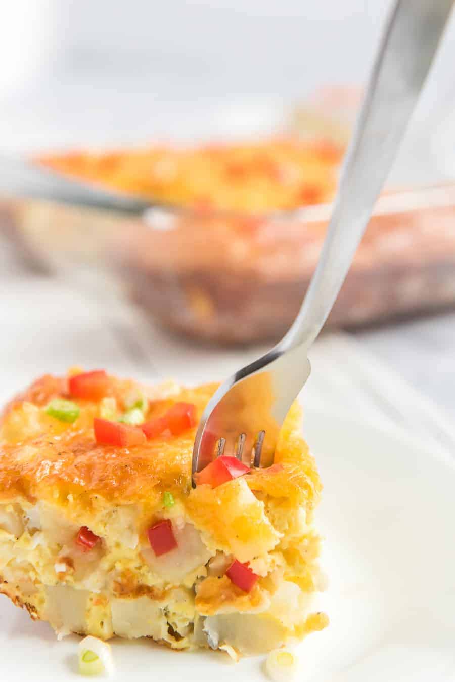 piece of egg and potato breakfast casserole with little pieces of red pepper and green onions sprinkled on top and silver fork.