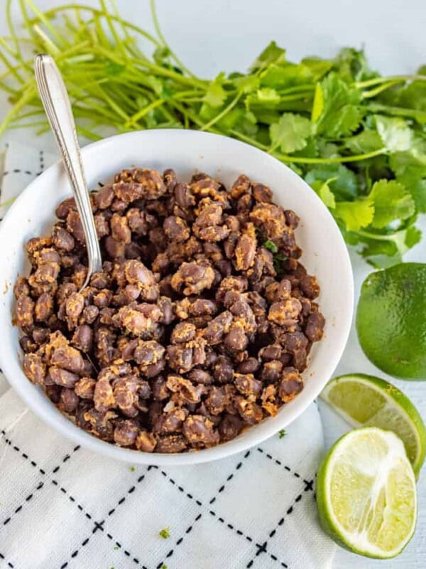 a bowl of black beans surrounded by limes and cilantro.