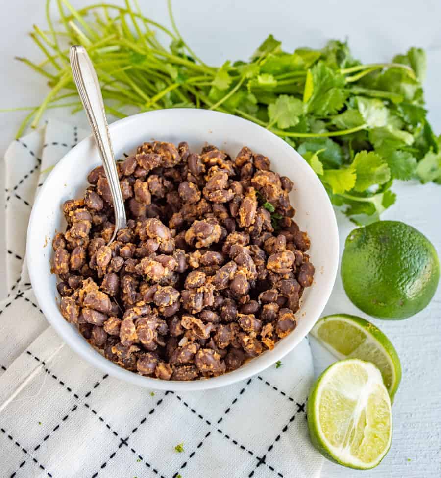 a bowl of black beans surrounded by limes and cilantro.