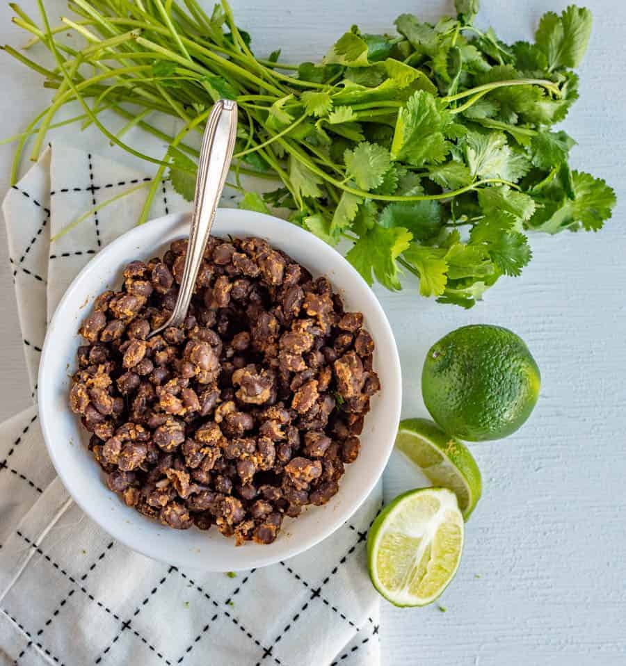 overhead shot of black beans surrounded by limes and cilantro.