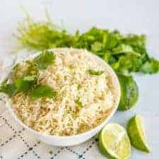 A bowl of cilantro lime rice topped with chopped cilantro and surrounded by cilantro and limes.