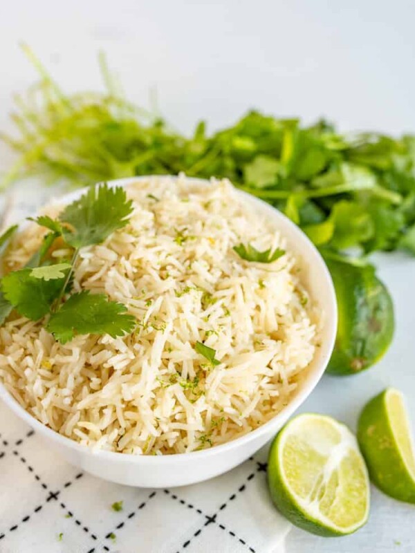 A bowl of cilantro lime rice topped with chopped cilantro and surrounded by cilantro and limes.