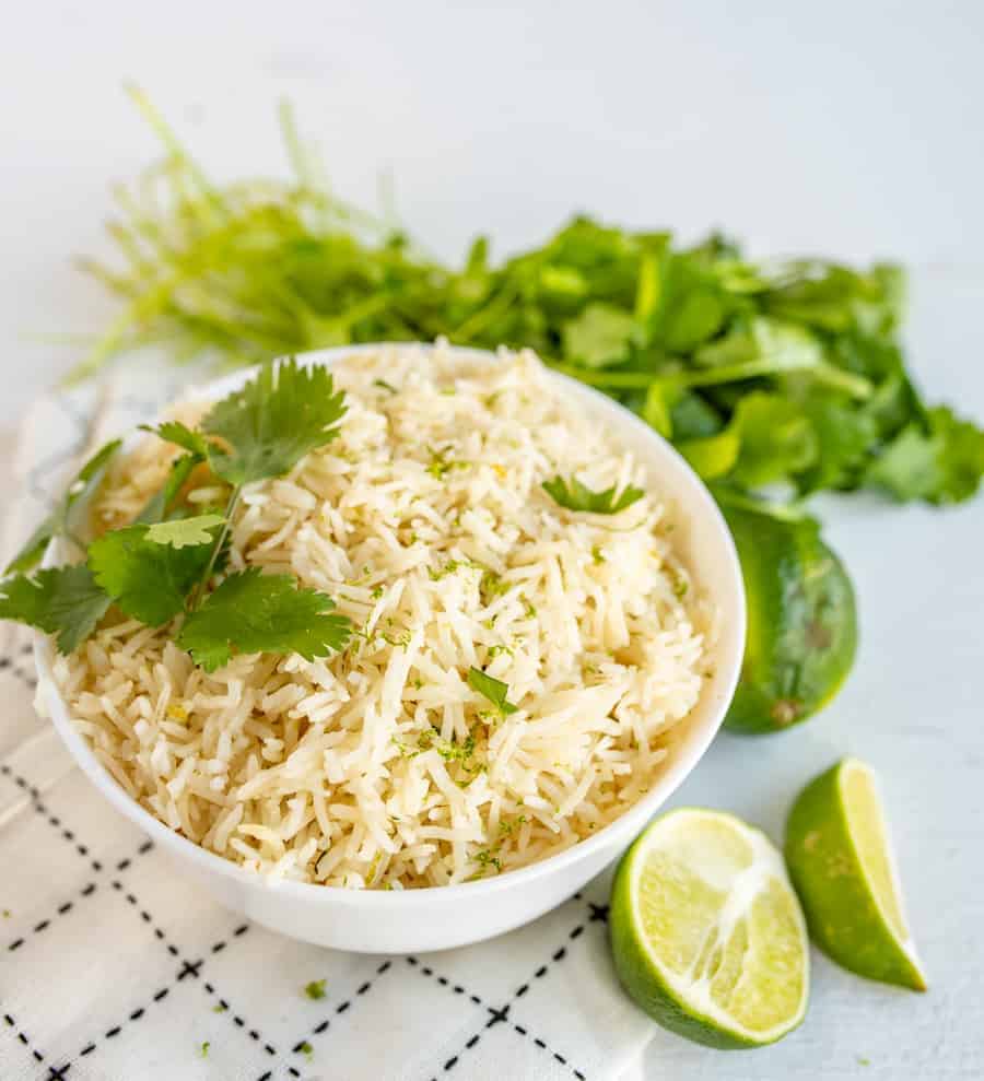 a bowl of cilantro lime rice topped with fresh cilantro. Bowl is surrounded by cilantro and limes. 