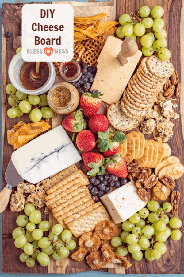 Title Image for DIY Cheese Board and a variety of cheeses, crackers, fruits, nuts and spreads on a wooden board