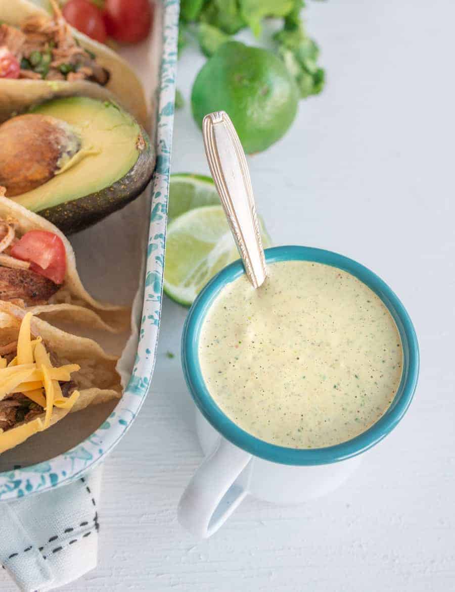 A bowl of creamy cilantro ranch dressing set next to a pan full of street tacos.