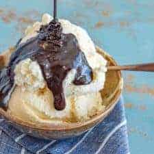 chocolate sauce in a metal pan on a black and white towel with a metal whisk.