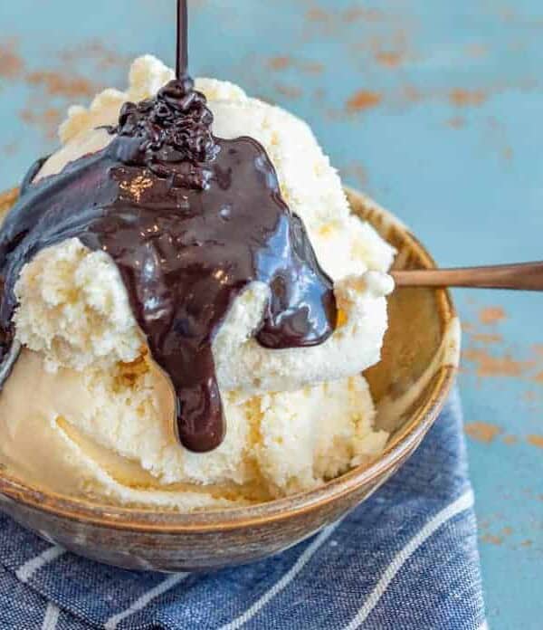 chocolate sauce in a metal pan on a black and white towel with a metal whisk.