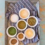 ingredients for homemade ranch dressing mix, spices in individual bowls on a blue and white striped towel set on a metal pan.