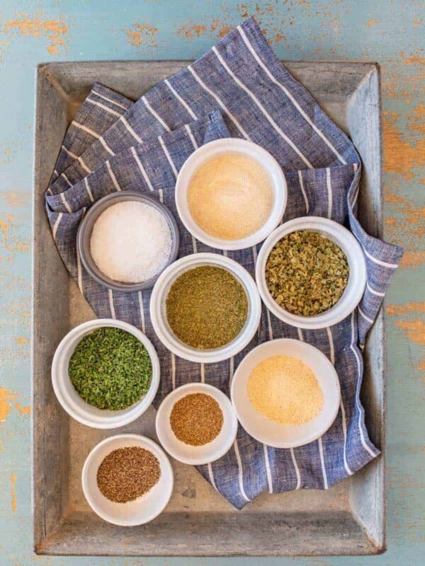 ingredients for homemade ranch dressing mix, spices in individual bowls on a blue and white striped towel set on a metal pan.