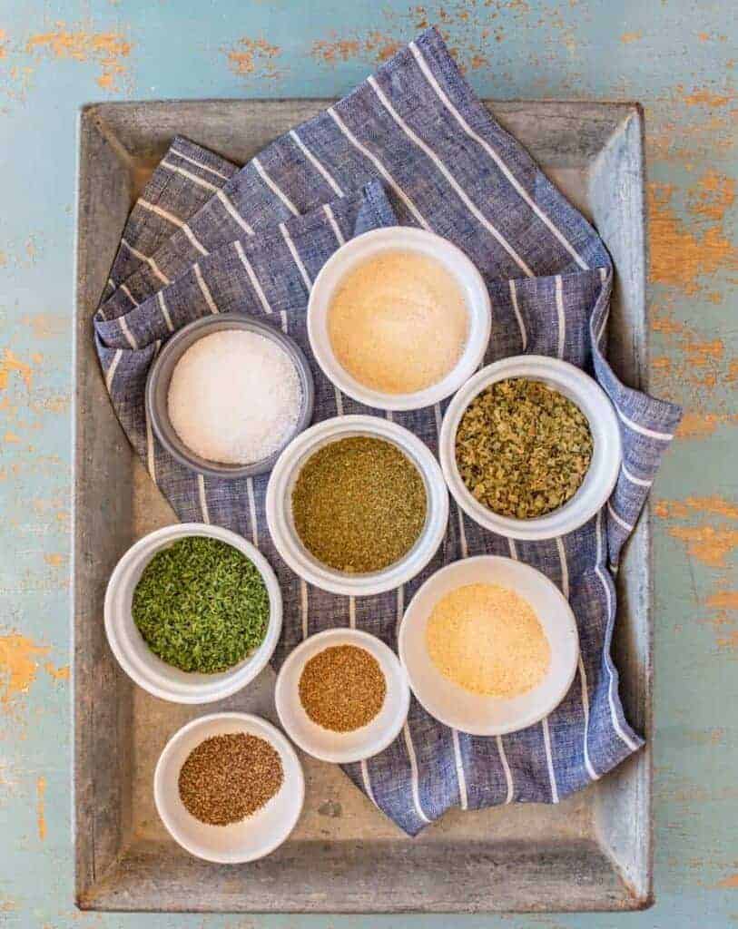 ingredients for homemade ranch dressing mix, spices in individual bowls on a blue and white striped towel set on a metal pan.