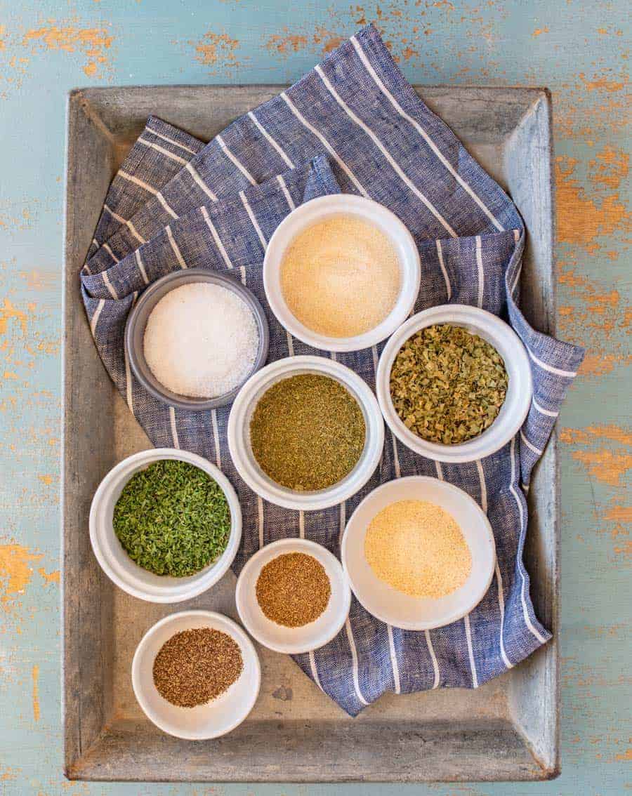 ingredients for homemade ranch dressing mix, spices in individual bowls on a blue and white striped towel set on a metal pan.