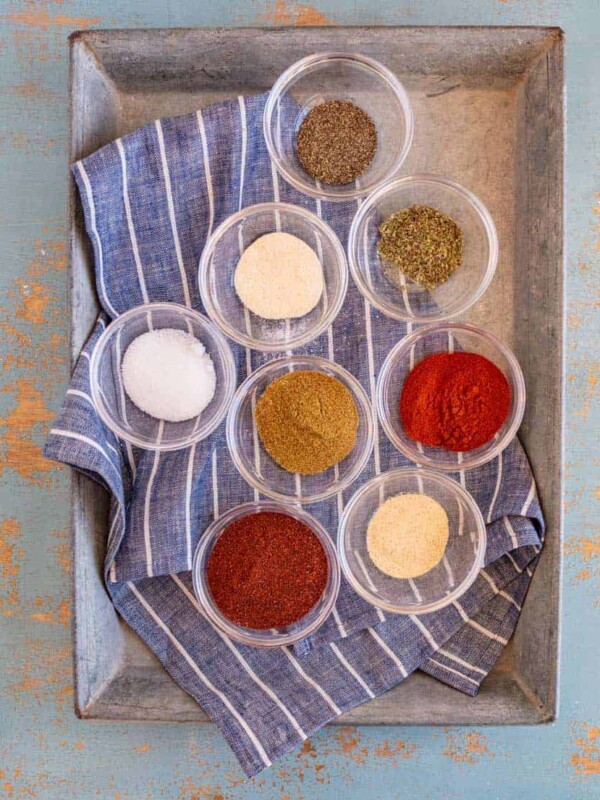 small clear glass bowls with different colored spices in each set in metal pan on top of blue and white striped towel.