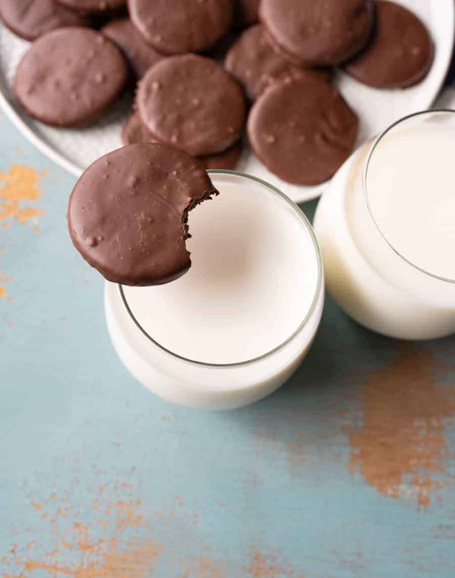round chocolate cookies on white plate with one cookie sitting on side of top of glass with white milk in it.