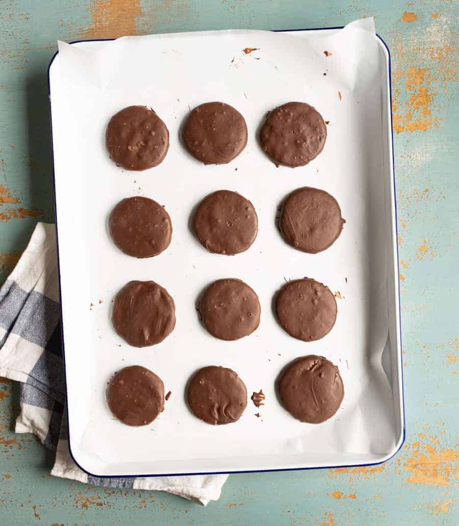 round chocolate cookies on white cookie sheet pan with blue and white checked towel under edge and on light blue background.