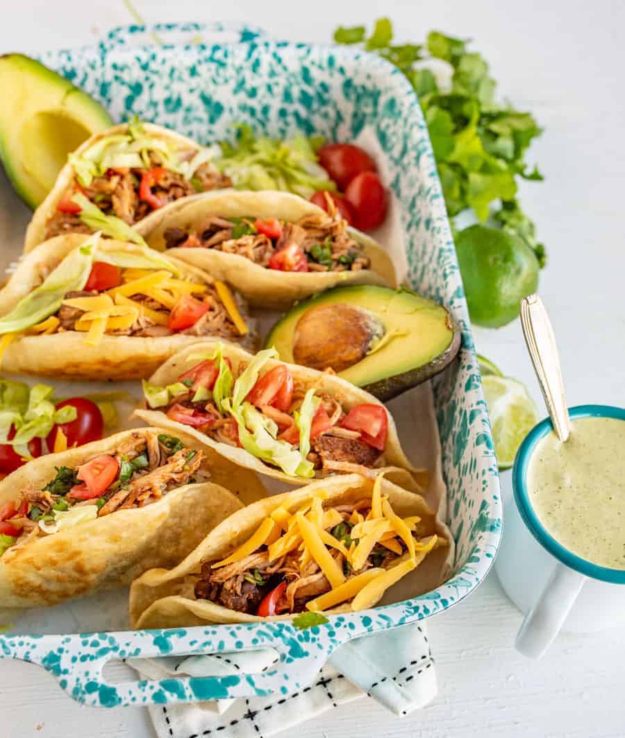 an overhead shot of corn tortilla shells filled with shredded chicken, cheese, and other taco toppings. 