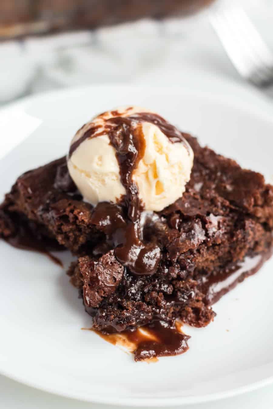 chocolate brownie dessert on a white plate with pale vanilla ice cream scoop on top and a drizzle of chocolate sauce.