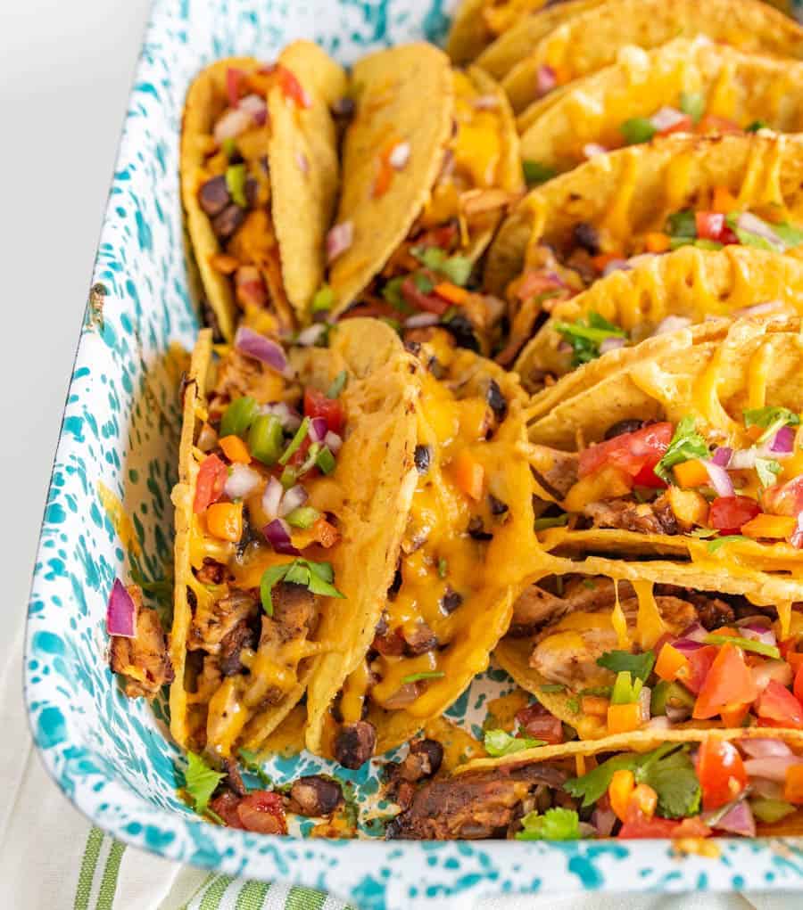 Crispy and Crunchy Baked Chicken Tacos are a quickly thrown-together and satisfying meal, complete with baked chicken, taco seasoning, black beans, hard taco shells, and plenty of shredded cheddar cheese.